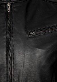 Svart läderjacka med en framträdande dragkedja framtill och en liten ficka med dragkedja på vänster bröst, med en slät yta och matt finish.