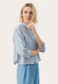 Lyseblå og hvid stribet skjorte med krave, optrukne ærmer og en lomme foran, parret med løse blå denim bukser.