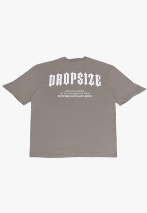 Grå oversized t-shirt lavet af bomuld. Har store hvide bogstaver på ryggen: "DROPSIZE" og et slogan nedenunder. Simplistisk rund hals.