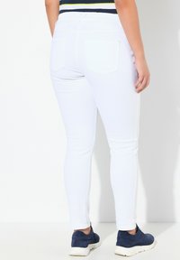 Jeans blancos ajustados con una textura suave, que cuentan con una cintura elástica, dos bolsillos traseros y un diseño de pierna cónica. Combinados con zapatillas azules.