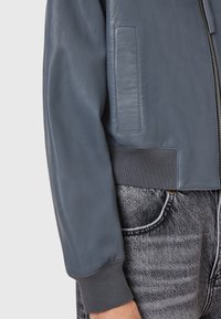 Giubbotto bomber in pelle grigia con polsini e fondo a coste, presenta una tasca laterale, una texture liscia e dettagli di hardware minimi.