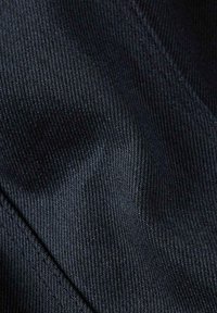 Primo piano di un tessuto denim nero, che mette in mostra la fine tessitura a spina di pesce e una leggera lucentezza, con cuciture visibili e sottili variazioni di texture.