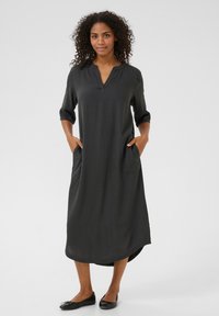 Robe mi-longue gris foncé avec un décolleté en V, des manches trois-quarts et deux poches latérales. Tissu lisse avec une coupe droite et un ourlet arrondi.