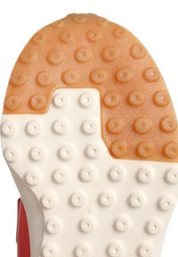 Suola di sneaker rossa con una superficie in gomma bianca e arancione texturizzata, caratterizzata da impugnature circolari per la trazione e una transizione tra i bordi liscia.