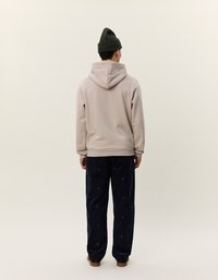 Beige hette med snøring i hetten og ribbede mansjetter, brukt sammen med marineblå bukser med et subtile sirkulært mønster. Mørk strikket lue på hodet.