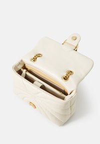 Baltas siuvinėtas odinis rankinukas su viršutiniu dangčiu, auksinėmis detalėmis ir vidiniais skyriais, įskaitant užtrauktuku uždaromą kišenę ir kortelių vietas.