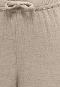 Gros plan sur un pantalon en tissu texturé beige avec une taille élastique et un cordon de serrage noué.