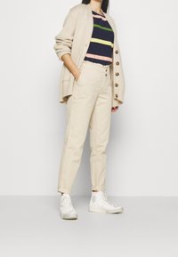 Beige pletený cardigan s velkými knoflíky, námořnický pruhovaný tričko s růžovými a zelenými pruhy, krémové zúžené kalhoty a bílé tenisky.