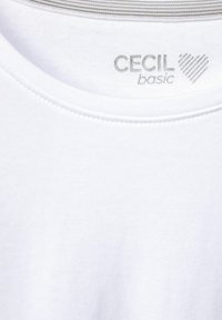 Witte katoenen T-shirt met een geribbelde halslijn, voorzien van een zilveren logo met de tekst "CECI basic" en een hartafbeelding. Glad textuur en een casual pasvorm.
