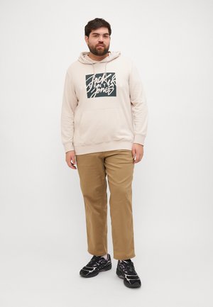 Felpa beige con stampa grafica, tasca frontale e cappuccio con cordoncino abbinata a pantaloni chinos color sabbia e sneakers nere. Tessuto dalla texture liscia.