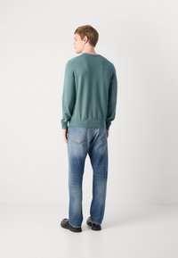 Green knitted sweater with long sleeves, crew neck, and ribbed hem, paired with light blue straight-leg jeans and black footwear.