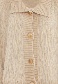 Cardigan beige con una texture morbida e fluffy, con sezioni in maglia a coste e bottoni color oro lungo la parte anteriore.