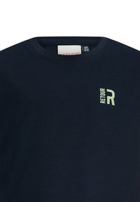 Granatowa bawełniana koszulka z okrągłym dekoltem i małym, jasnozielonym logo "RET OUR" na lewej piersi. Gładka tekstura.