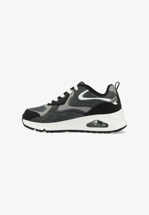 Zapatilla deportiva gris con acabado liso, detalles en negro contrastante, cordones blancos y una unidad de amortiguación de aire visible en la suela.