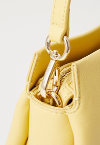 Borsa a mano in finta pelle gialla con zip e dettagli in metallo dorato. Presenta una forma strutturata e cuciture visibili lungo i bordi.