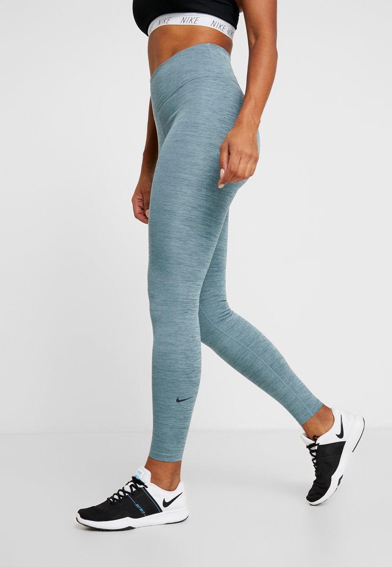 Donna che indossa leggings a vita alta di colore blu chiaro, reggiseno sportivo nero con il logo Nike e scarpe da corsa Nike in bianco e nero mentre cammina.