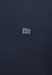 Tissu tricoté bleu marine avec un petit symbole brodé ressemblant à un drapeau en fils bleu clair et blanc au centre.