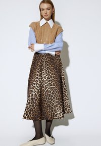 Chaleco de punto beige sobre una camisa azul claro con cuello blanco, combinado con una falda marrón con estampado de leopardo y bailarinas crema.