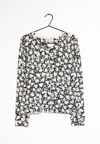 Maglietta a maniche lunghe in bianco e nero con motivo floreale, colletto tondo e orlo dritto, realizzata in un tessuto leggero, appesa a un gancio.