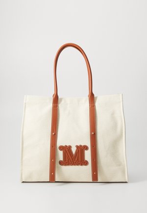 Canvas tote bag in cream with brown leather straps and a prominent embossed "M" logo on the front. Features reinforced stitching.