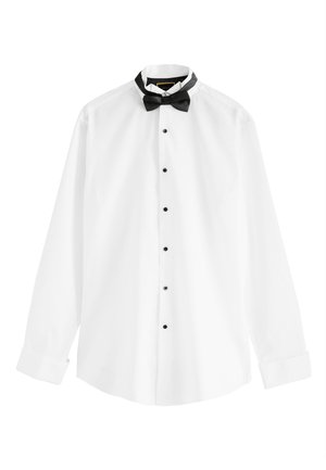 Férfi igazít egy ezüst mandzsettagombot egy fehér ing mandzsettáján, amelyen fekete gombok láthatók az ing elején.