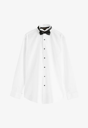 Férfi igazít egy ezüst mandzsettagombot egy fehér ing mandzsettáján, amelyen fekete gombok láthatók az ing elején.