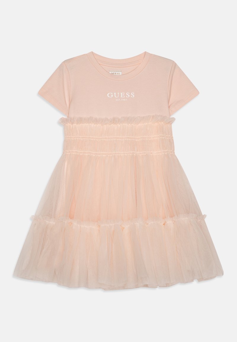 Robe courte à manches courtes rose pâle avec le texte "GUESS EST. 1981" sur la poitrine et jupe en tulle superposée avec détails à volants.