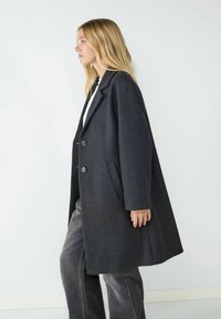 Grau wollmix Mantel mit Revers, zwei Frontknöpfen, Seitentaschen und entspannter Passform, kombiniert mit dunklen Jeans.