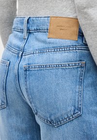 Ανοιχτό μπλε τζιν με πίσω τσέπες και καφέ δερμάτινη ετικέτα με την επιγραφή «perfect jeans», φορεμένο με γκρι τοπ.