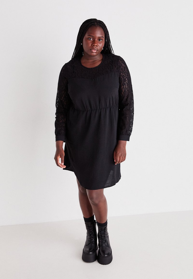 Robe noire avec un design à manches longues en dentelle, taille froncée et coupe décontractée. Associée à des bottes à plateforme noires épaisses. Texture lisse.
