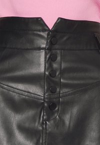 Jupe en cuir noir avec une taille structurée, présentant un design en V, cinq boutons noirs et des détails de couture diagonale.