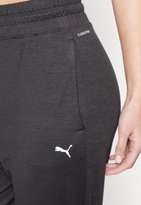 Czarne spodnie sportowe wykonane z miękkiego materiału, z elastycznym paskiem i białym logo Puma na udzie. Minimalistyczny design z kieszeniami.