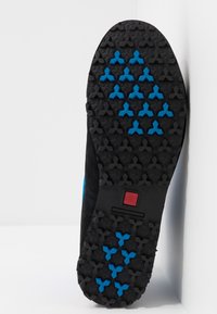 Černá podrážka boty s texturovaným gumovým povrchem a modrými hvězdicovými akcenty, zobrazující geometrický vzor dezénu pro lepší přilnavost.
