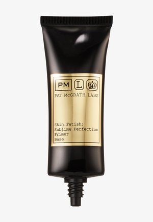 Tube en plastique noir avec une étiquette dorée, comportant du texte noir. Le produit est une base intitulée "Skin Fetish : Sublime Perfection."