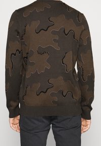 Brauner Camouflage-Pullover mit schwarzen Akzenten, der ein strukturiertes Muster und gerippte Bündchen aufweist. Entworfen in einer regulären Passform mit Rundhalsausschnitt.