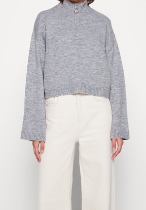 Grijze, gebreide cropped sweatshirt met een hoge kraag en een rits aan de voorkant. Ribbenboorden aan de mouwen en onderkant. Gecombineerd met off-white wijde jeans.