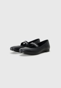 Sapatilhas de couro preto com bico redondo, apresentando uma faixa cruzada com "VALENTINO" em texto branco. Textura suave e design de salto baixo.