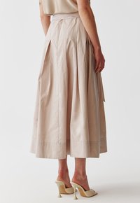 Vaalean beige, laskostettu maksihame korkealla vyötäröllä ja sileällä pinnalla, yhdistettynä kermaisiin korkokenkiin.