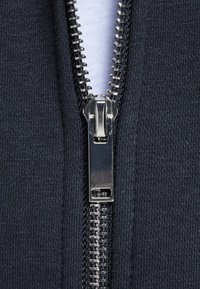 Tela de color marino con un zipper metálico plateado, ubicado en el centro, que muestra una textura suave y un detalle de dientes entrelazados.