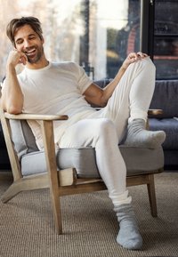 Lett og beige loungewear, inkludert en t-skjorte med korte ermer og tettsittende bukser, paret med grå sokker. Stol med tresramme og myk grå pute.