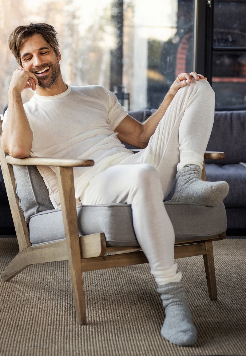 Lett og beige loungewear, inkludert en t-skjorte med korte ermer og tettsittende bukser, paret med grå sokker. Stol med tresramme og myk grå pute.