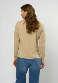 Beige langledige shirt gemaakt van zachte stof, met een relaxte pasvorm en een ronde zoom, gecombineerd met blauwe wijde jeans.