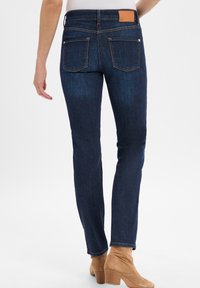 Dunkelblaue Denim-Jeans mit einer figurschmeichelnden Passform, sichtbaren Gesäßtaschen und einem hellbraunen Lederlabel an der Taille. Weicher Stoff mit minimalen Verfärbungen.