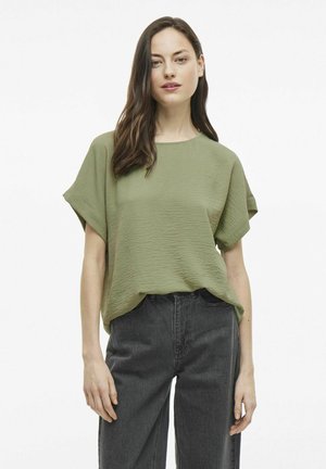 Olivenfarvet top med korte ærmer og en tekstureret overflade, parret med højhalsede mørkegrå jeans. Simpel, afslappet pasform med en rund halsudskæring.