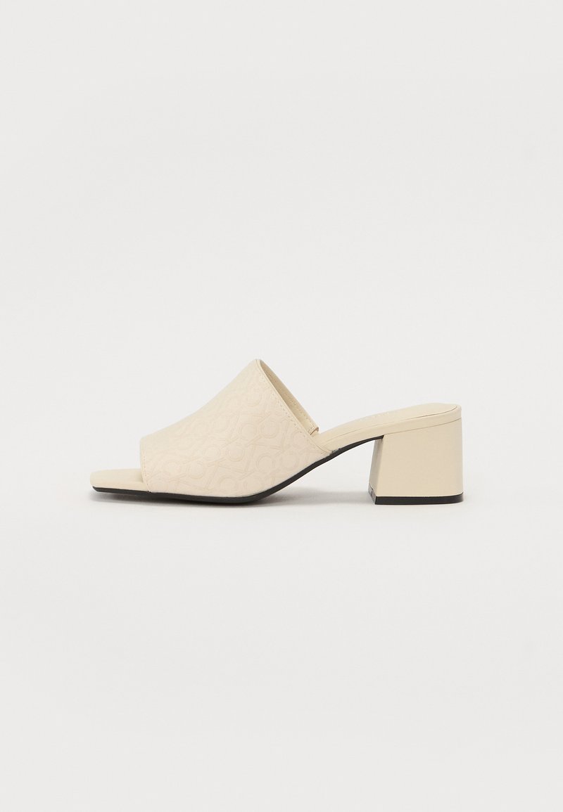 Mules beiges à talons carrés et à bout ouvert, dotés d'un dessus à motifs et d'une finition lisse. Talon carré avec une légère accentuation noire à la base.