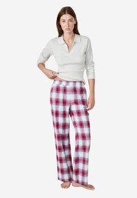 Lichtgrijze, geribbelde trui met een kraag; rood-blauwe geruite flanelbroek met elastische tailleband; relaxed fit; blootvoets.