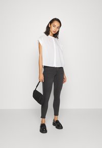 Witte kortemouwen overhemd, grijze skinny jeans, zwarte schoudertas en zwarte schoenen met een glanzende afwerking. Eenvoudig, gestroomlijnd ontwerp.