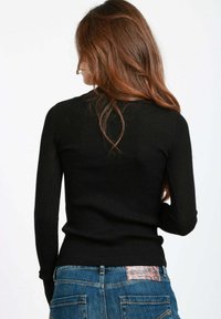 Maglione a maniche lunghe nero a coste con un design aderente, tessuto testurizzato e scollatura a girocollo, abbinato a jeans in denim blu con tasche posteriori.