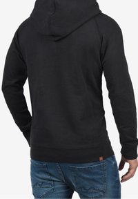 Sudadera negra con capucha ajustable, puños y dobladillo acanalados, fabricada en una tela suave. Presenta una pequeña etiqueta de logo cerca del dobladillo.