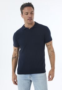 Polo navy de cuello tipo camisa y mangas cortas, fabricado en una tela suave y elástica. Presenta un dobladillo acanalado y un diseño minimalista.